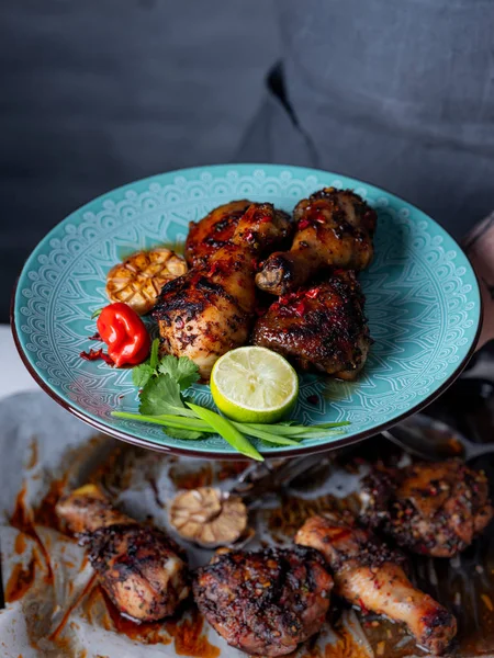 Bir tabak taze pişmiş baharatlı tavuk budu ile tutan adam Görünümü Kapat sarımsak, biber biber, limon dilimi ve otlar ile hizmet 