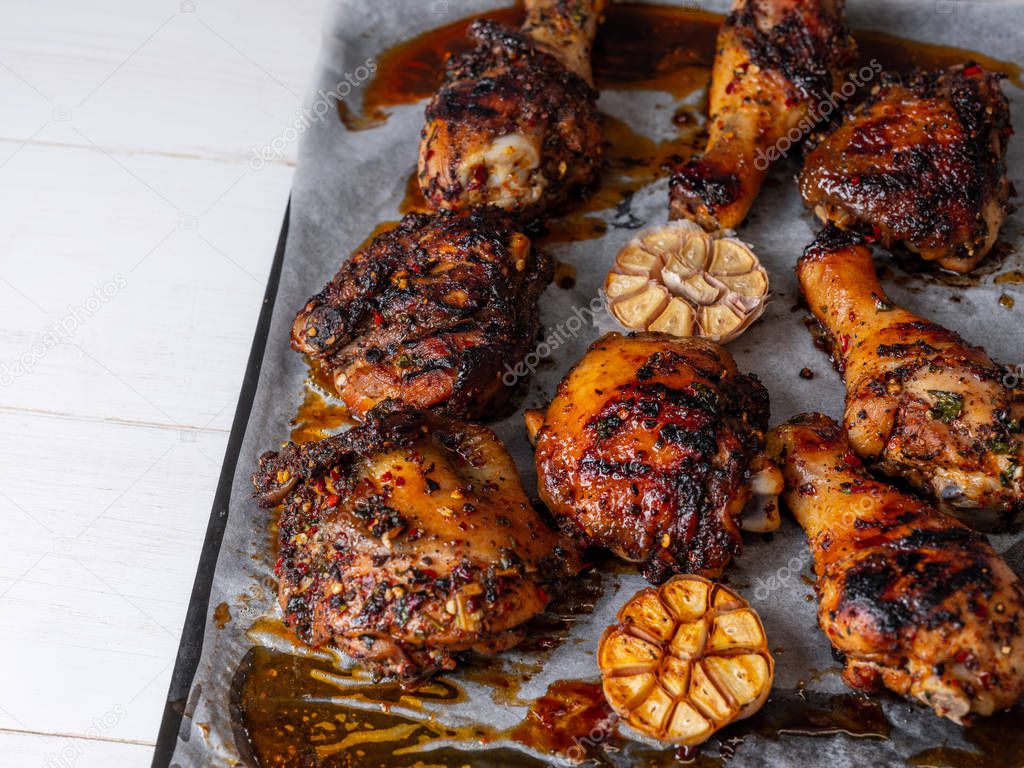 Close view of fresh baked chicken legs spices and garlic on baking pan on white background 