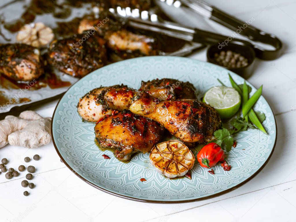 Fresh baked chicken legs served with lime slice, herbs and garlic on blue plate