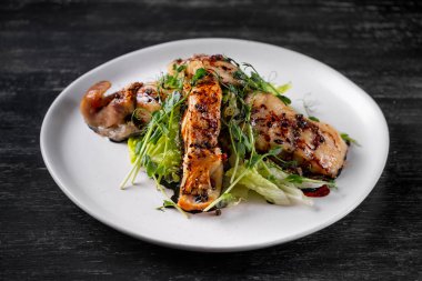 Pişmiş balık dilimleri ile baharat soslu beyaz plaka üzerinde yeşil salata ile servis