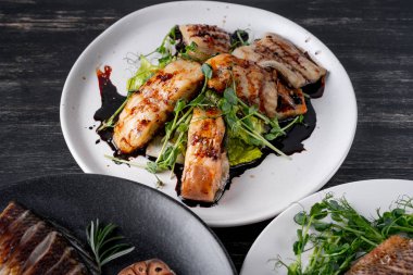 Fırında Balık yemekler çeşitli beyaz ve siyah plakalar üzerinde yeşil salata ile servis