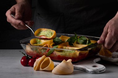 Yeşil pesto sos ile doldurulmuş lumaconi kaşıkla Beyaz Ahşap doğrama tahtası üzerinde tutarak Şef Görünümü Kapat