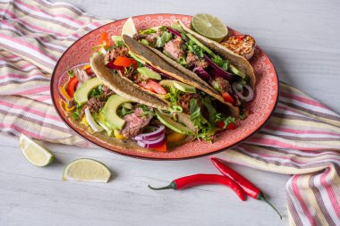 Beyaz ahşap arka plan üzerinde kireç dilimi ile servis sığır eti, avokado dilimleri ve biber ile taze tacos 