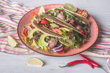 Beyaz ahşap arka plan üzerinde kireç dilimi ile servis sığır eti, avokado dilimleri ve biber ile taze tacos 