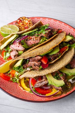 Beyaz ahşap arka plan üzerinde kireç dilimi ile servis sığır eti, avokado dilimleri ve biber ile taze tacos 