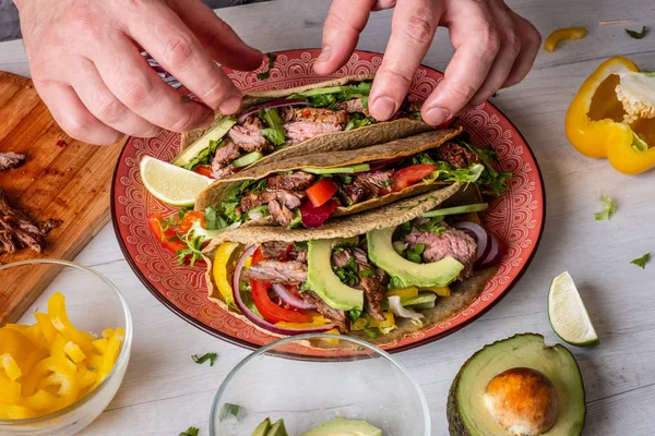 Fresh tacos with beef, avocado slices and peppers served with lime on white wooden background