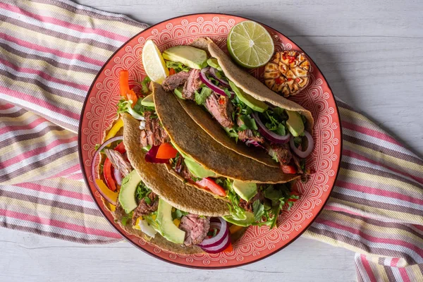 Beyaz ahşap arka plan üzerinde kireç dilimi ile servis sığır eti, avokado dilimleri ve biber ile taze tacos 