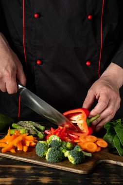 Ahşap doğrama tahtasına kırmızı biber dilimleyen erkek şefin yakın görünümü