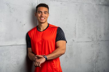 Kırmızı tişörtlü genç adam gri beton arka planda poz veriyor. 