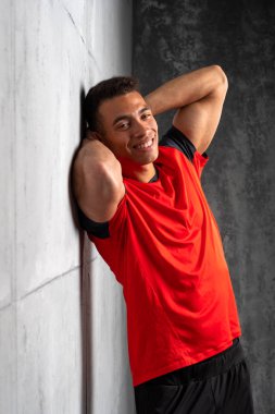 Kırmızı tişörtlü genç adam gri beton arka planda poz veriyor. 