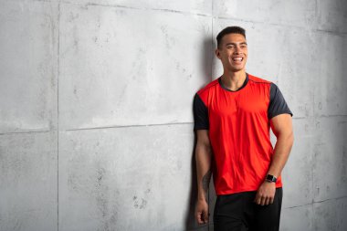 Kırmızı tişörtlü genç adam gri beton arka planda poz veriyor. 