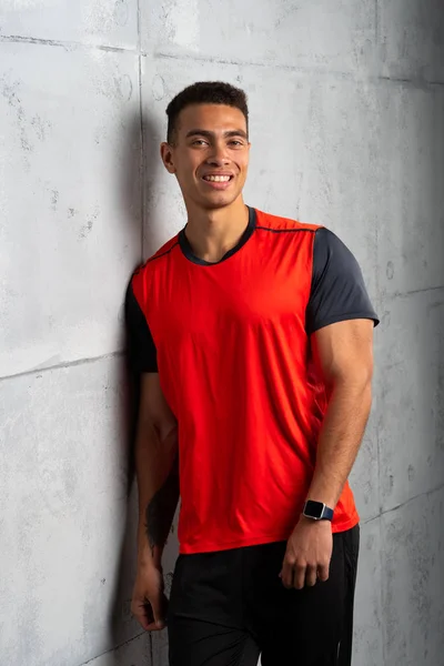 Young sporty man in red t-shirt posing on grey concrete background
