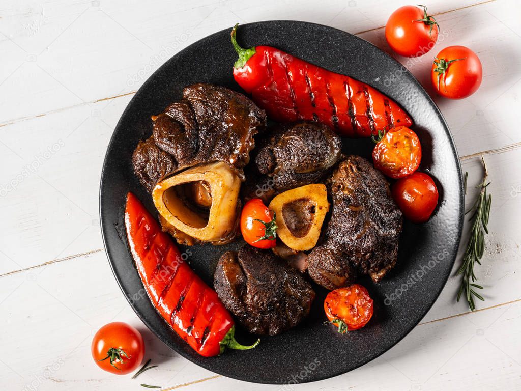 Top view of cooked meat with vegetables on black plate standing on white wooden table 