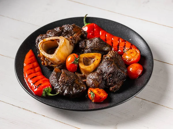 Grilled beef with season vegetables on black plate standing on white wooden table