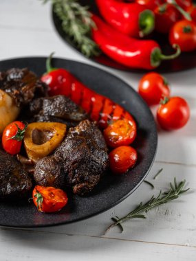 Beyaz ahşap masa üzerinde duran siyah tabak üzerinde sebze ile ızgara et yakın görünümü 