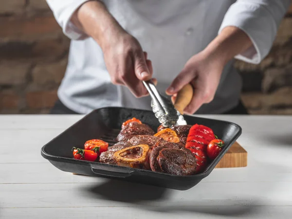 Man grilling steaks and vegetables on grill pan on wooden table