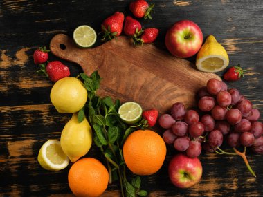 Tahta kesme tahtasının etrafında duran taze meyve salatası malzemelerinin üst görüntüsü.