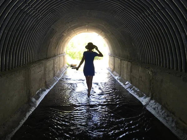 girl walking barefoot through the water in a dark tunnel to the