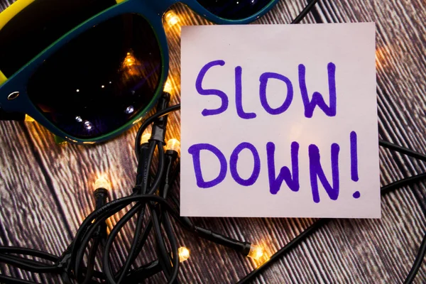 Yavaş aşağı mavi renk ile hafif pembe Not kağıt üzerinde el yazısı. Ahşap arka plan ile farklı renklerde iki güneş gözlüğü ve birkaç ışık yayılır. Uyarı ve öneri iş kavramı. 