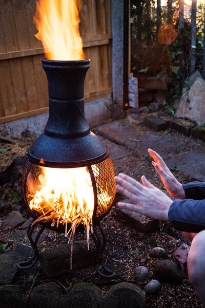 Wooden camp fire in the night. Preparing barbecue fire in the outside. Man sitting by the open fire and firing with wood twigs. Camping fire in the twilight night