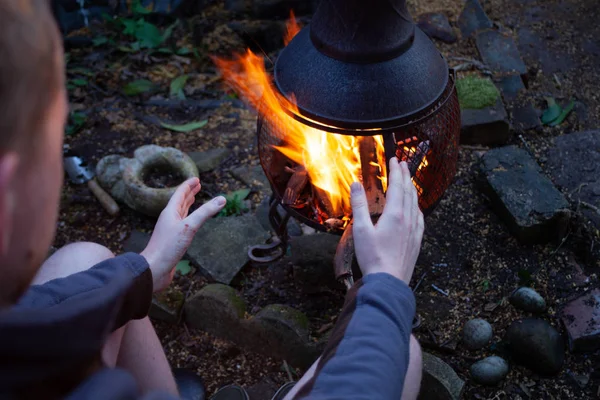 野营火和人在黑暗的暮光穆迪照片 那人在开火前用手取暖 露营概念与户外明火火焰 准备烧烤火 — 图库照片