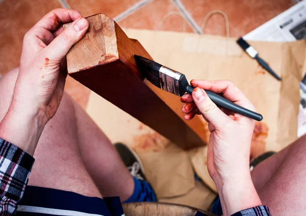 Top view of hands holding painting brush. Closeup view of home renovating and old furniture painting. Man holds painting brush and paints wooden board