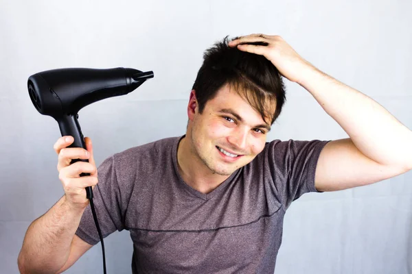 Genç adam, vantilatör ile saç kurur. Bir saç kesimi için bir gece hayatı gidiş için hazırlanıyor. Saç üfleyici tutan adam. Onun saç kurur iken gülümseyen genç.