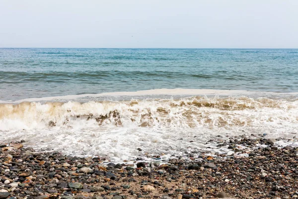海滩边多云的一天 海浪拍打着海岸 蓝天无云 夏天概念以海浪 海浪上的海沫 岩石海滩与五颜六色的石头 — 图库照片