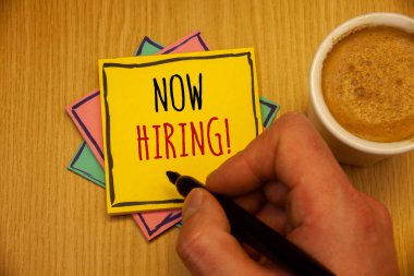 Şimdi işe motivasyonel arama gösterilen metin işareti. Kavramsal fotoğraf işgücü istedim çalışanlar Recruitmentman sarı oluşturma pembe mavi kağıtları siyah tutan el kahve kalem