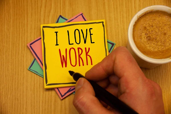 Text sign showing I Love Work. Conceptual photo To be happy satisfied with job Be doing what you most likeMan creating yellow pink blue papers Hand holding black pen cup of coffee