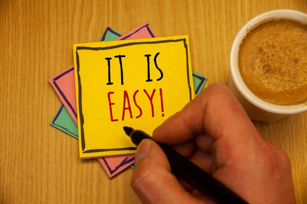 Text sign showing It Is Easy Motivational Call. Conceptual photo Clear Simple Not complicated Basic EffortlessMan creating yellow pink blue papers Hand holding black pen cup of coffee