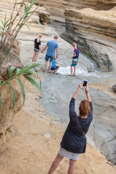 Woman taking candid photo. Parents holding hands while watching the son enjoying the water flowing from the cliff. Family bonding moments and travel get away