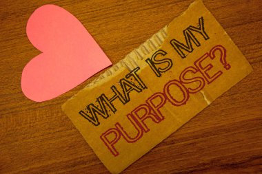 Text sign showing What Is My Purpose Question. Conceptual photo Direction Importance Discernment Reflection Peru color torn page with engraved black red text woody desk pink heart clipart