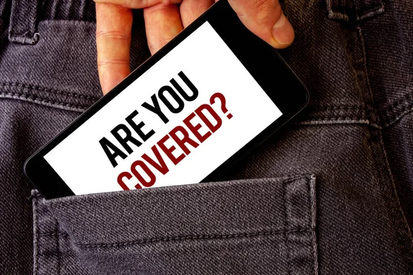Conceptual hand writing showing Are You Covered Question. Business photo showcasing Have a Security and Health Insurance Medical Care Man holding cell phone white screen letters jeans pocket