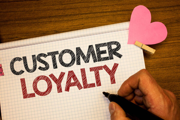 Writing note showing  Customer Loyalty. Business photo showcasing Client Satisfaction Long-Term relation Confidence Man holding pen ideas notebook pink heart letters on wooden background