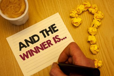 Conceptual hand writing showing And The Winner Is . Business photo showcasing Announcing as first place in competition or race Wooden desktop hand hold marker page coffee question mark clipart