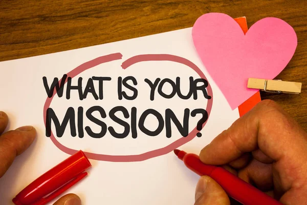 Handwriting text What Is You Mission Question. Concept meaning asking someone about his plans and to-do list Human hand retain red pen circled black words paper hook rivet pink heart