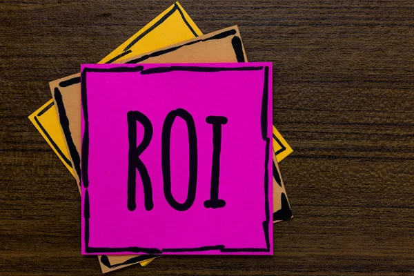 Writing note showing Roi. Business photo showcasing Return on investment performance measure gains business growth Three art small paper two yellow one pink wood brown lite grey shadow