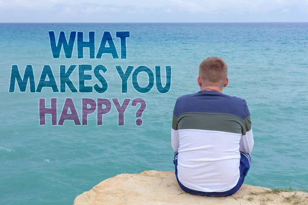 Writing note showing  What Makes You Happy Question. Business photo showcasing Happiness comes with love and positive life Man sitting sand watching beach Message Relax reflection intention