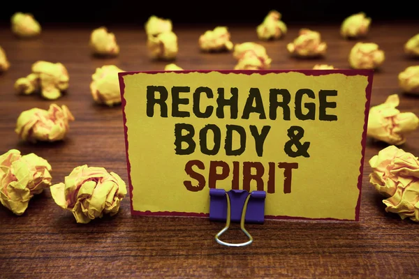 Handwriting text writing Recharge BodyandSpirit. Concept meaning fill your energy through relaxation and having fun Yellow sticky card clipped text notice crumpled paper balls wood table