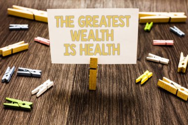 En büyük zenginlik sağlık olduğunu gösteren metin işareti. Kavramsal fotoğraf sağlıklı olmanın ödülü Take care Clothespin holding beyaz kağıt Not birkaç clothespins ahşap zemin olduğunu