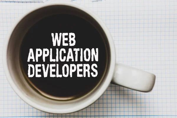 Writing note showing Web Application Developers. Business photo showcasing Internet programming experts Technology software Coffee mug with black coffee floating some white texts on white paper
