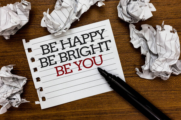 Text sign showing Be Happy Be Bright Be You. Conceptual photo Self-confidence good attitude enjoy cheerful Paper lumps laid randomly around white notepad touch black pen on woody floor