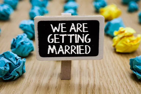 Text sign showing We Are Getting Married. Conceptual photo Engagement Wedding preparation Loving couple Paperclip hold written chalkboard behind paper lumps on woody deck