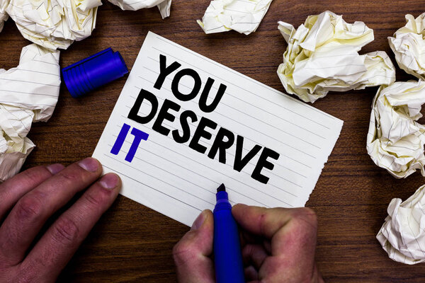 Writing note showing You Deserve It. Business photo showcasing Reward for something well done Deserve Recognition award Hand holding marker write words paper lob scatter around woody desk