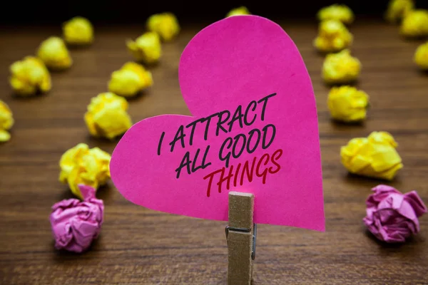 Text sign showing I Attract All Good Things. Conceptual photo Positive attraction law Motivation Affirmation Paperclip hold pink heart with text blurry paper lobs on wooden floor