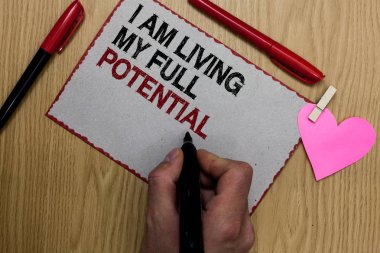 Text sign showing I Am Living My Full Potential. Conceptual photo Embracing opportunities using skills abilities Written sticky note clip pinch heart hand hold marker red pen on wooden desk clipart