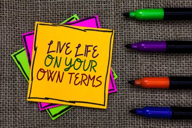 Text sign showing Live Life On Your Own Terms. Conceptual photo Give yourself guidelines for a good living Written on some colorful sticky note 4 pens laid in rank on jute base clipart