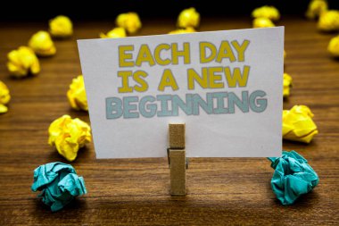 Writing note showing Each Day Is A New Beginning. Business photo showcasing Every morning you can start again Inspiration Written notepad stand with paperclip yellow blue lobs on wooden deck clipart