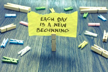 Handwriting text Each Day Is A New Beginning. Concept meaning Every morning you can start again Inspiration Paperclip hold written torn page many clips laid on bluish wooden floor clipart